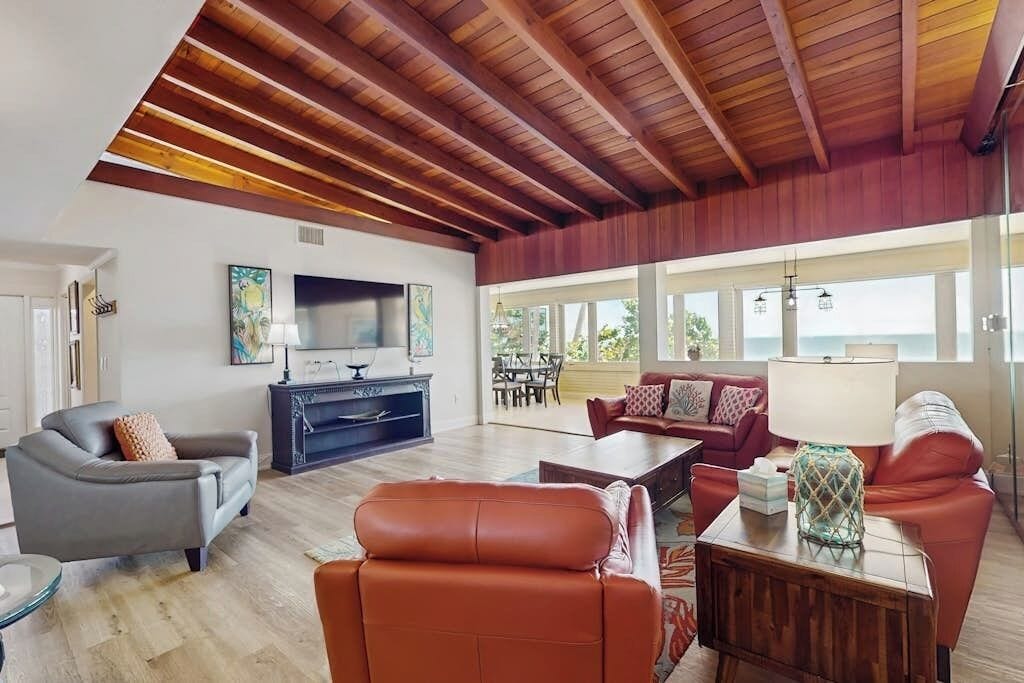 Un vaste espace de vie doté d’un plafond en bois, d’un téléviseur et d’un coin salon comprenant un canapé et des fauteuils.