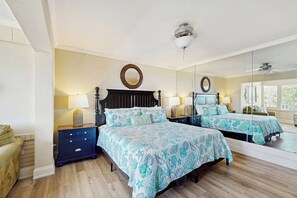 A bedroom with two beds, a large mirror, bedside lamps, and a wooden floor.