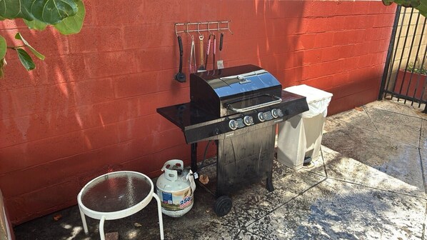 A barbecue grill with a gas tank and a table nearby.
