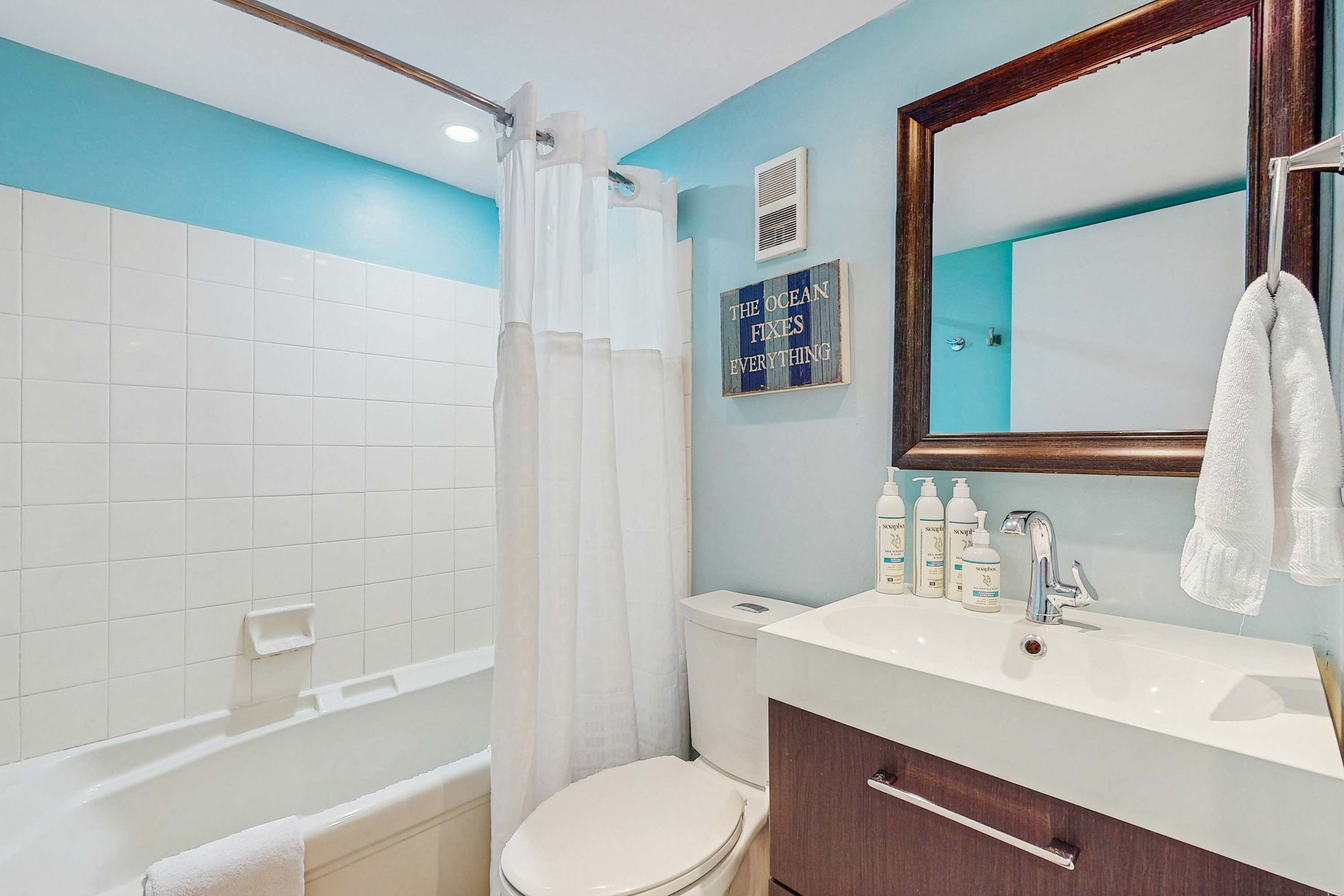 Un baño con bañera, inodoro y lavabo. Hay una toalla colgada en la pared y un letrero que dice 'The Ocean Fixes Everything'.