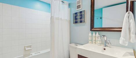 Un baño con bañera, inodoro y lavabo. Hay una toalla colgada en la pared y un letrero que dice 'The Ocean Fixes Everything'.