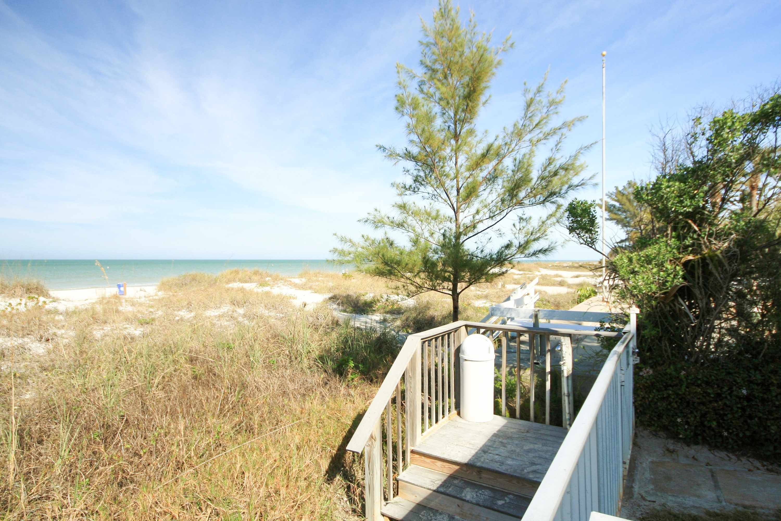 A wooden staircase leading to a beach area with a clear view of the ocean and a tree.