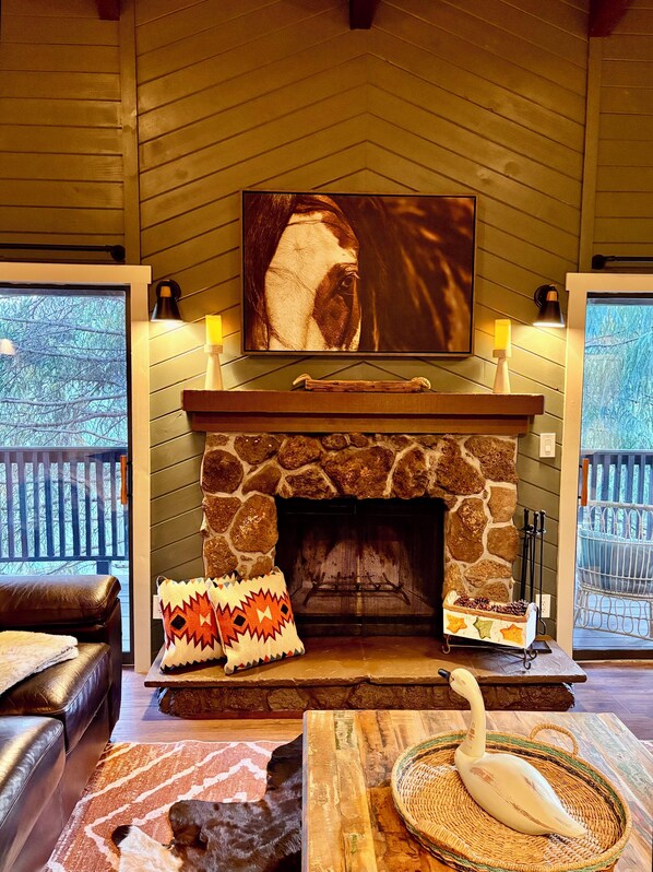 A cozy living room with a stone fireplace, a mounted TV, and a comfortable seating area with a dog and a decorative swan. - Golf & Ski Get-away Pinetop (Pinetop-Lakeside)