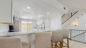 A modern kitchen with a central island, bar stools, and a staircase with a black railing. - Spacious and dog friendly close to the Gulf and beaches AC WIFI and WD (Treasure Island)