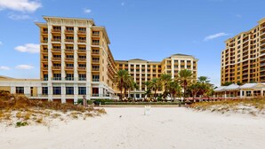 Un hotel frente a la playa con varias edificaciones, palmeras y una playa de arena.