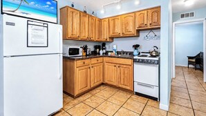 A compact kitchen with wooden cabinets, a white refrigerator, a microwave, a stove, and a small sink.