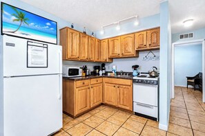 Una cucina compatta con mobili in legno, un frigorifero bianco, un forno a microonde, un fornello e un lavandino piccolo.