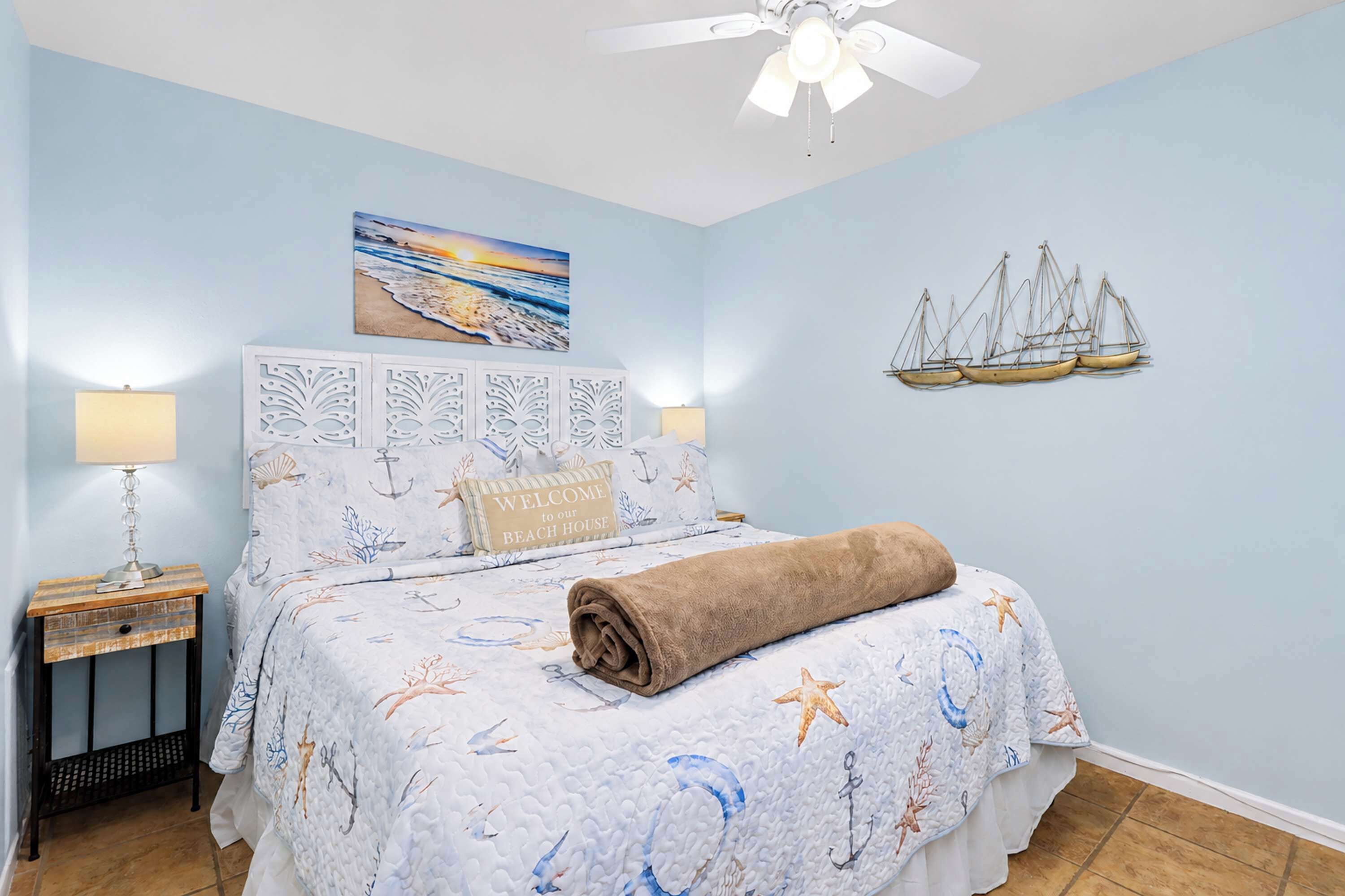 A bedroom with a bed, nightstands, a ceiling fan, a painting, and wall decor.