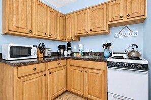 A kitchen with wooden cabinets, a microwave, a toaster, a coffee maker, a kettle, and a stove. - Charming Gulf front condo with views of Belleair Beach with central AC (Belleair Beach)