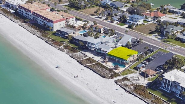 An aerial view of a coastal residential area with houses, a road, and a beach.
