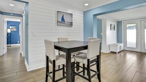 A dining area with a dark wooden table and white chairs, a sailboat painting on the wall, and a view through a glass door. - Stunning centrally located home with enclosed yard patio grill WD and AC (Largo)