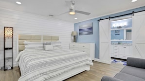 A bedroom with a bed, a ceiling fan, a nightstand, a lamp, and a view of the bathroom. - Stunning centrally located home with enclosed yard patio grill WD and AC (Largo)