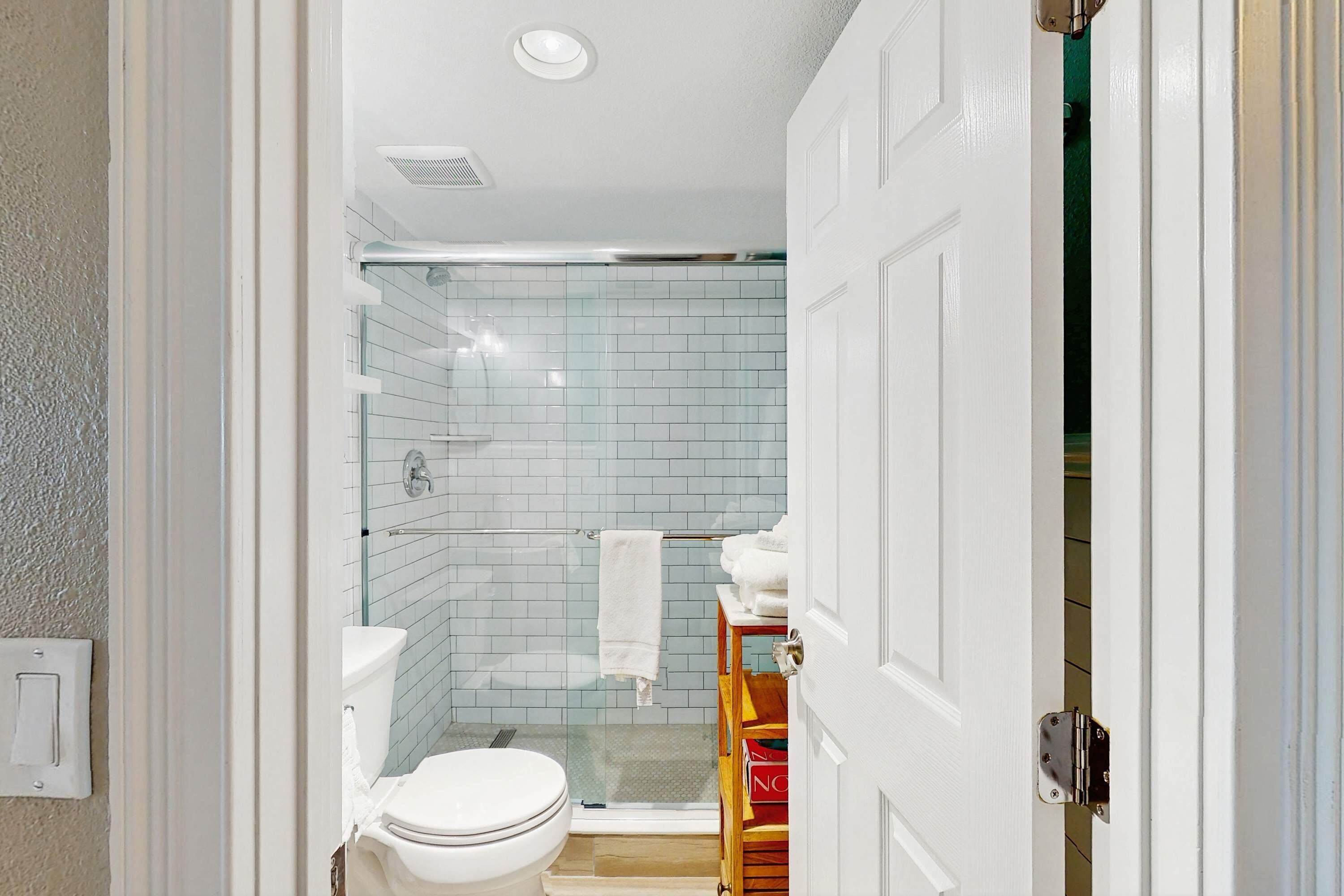 A bathroom with a glass shower enclosure, a white toilet, and a wooden shelf with towels.