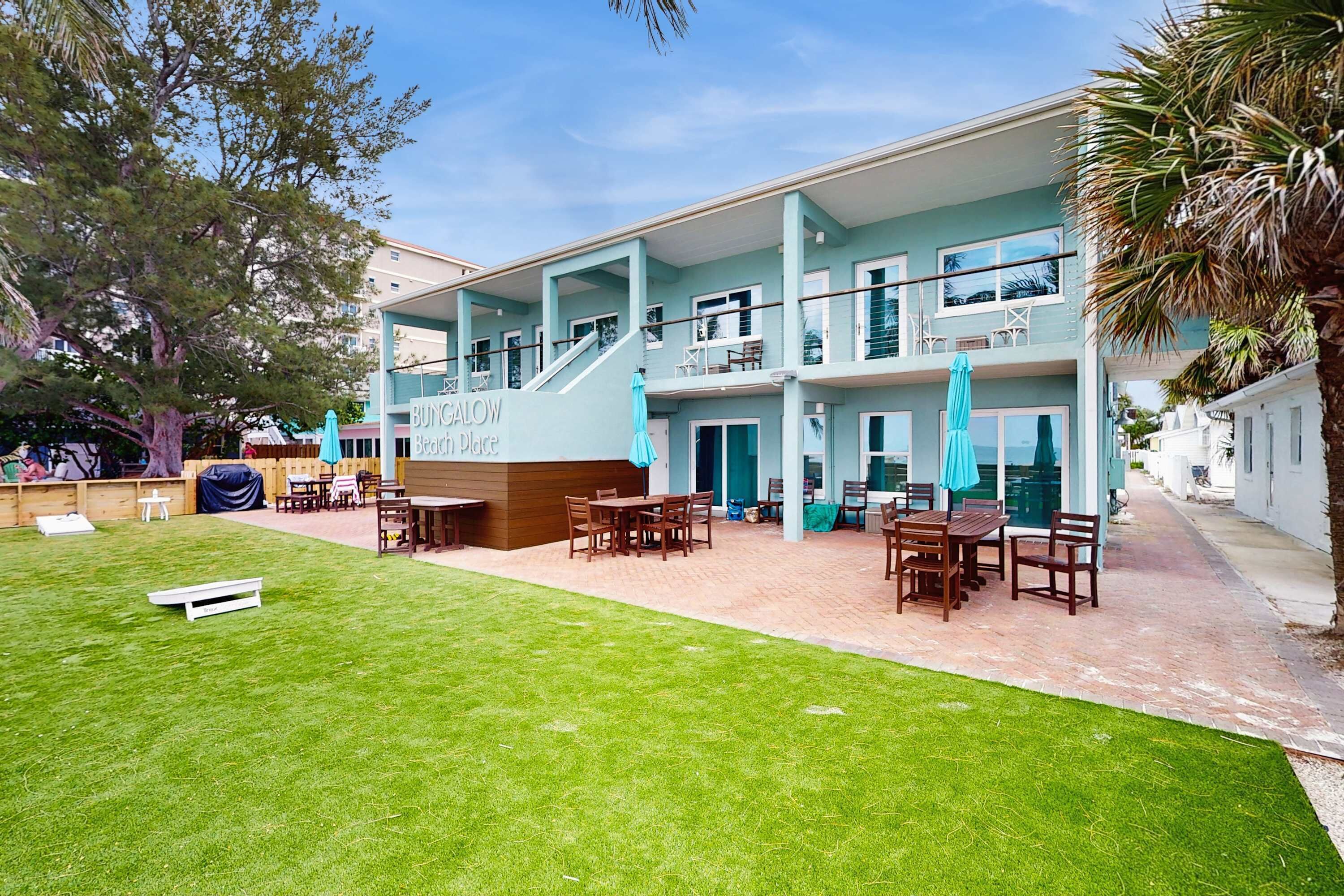 Un bâtiment à deux étages, sur lequel on peut lire l’inscription « ACHETEZ CALOW Beach Resort ». Il y a des espaces de détente en plein air avec des tables et des chaises, ainsi qu’une pelouse devant le bâtiment.