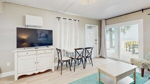 A living room with a television, a dining table, and chairs. There is a window with curtains, a ceiling fan, and a view of the outside. - Gulf front condo with full kitchen and central AC (Indian Shores)