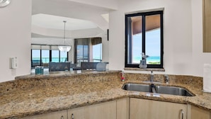 Una cocina moderna con encimeras de granito, un lavamanos de acero inoxidable y un amplio ventanal con vistas al mar.