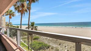 Un balcón con vista a una playa, palmeras y un cielo despejado.