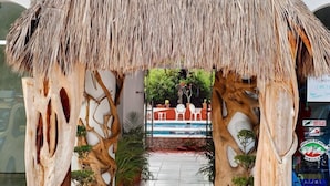 Entrada com telhado de palha e design de madeira único, plantas em vasos e vista clara do interior.