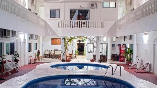 Uma grande piscina interior com uma escadaria central, rodeada por várias varandas com grades e janelas.