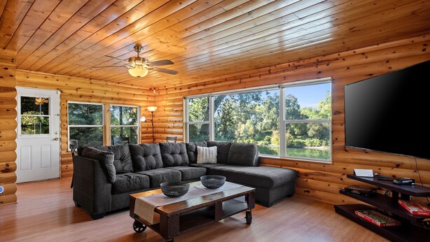 Een houten blokhut interieur met een houten plafond, een grote televisie, een grijze hoekbank en een houten salontafel.