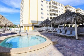 Ein Poolbereich mit Liegestühlen und Reedsondenschirmen, umgeben von einem mehrstöckigen Hotelgebäude.