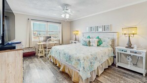 Ein Schlafzimmer mit Bett, Schreibtisch, Stuhl, Deckenventilator und einem Fenster mit Jalousien.
