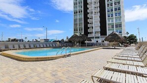 Ein Schwimmbecken mit Liegestühlen und einem hohen Gebäude im Hintergrund.