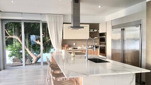 Una cocina moderna con una isla grande, electrodomésticos de acero inoxidable y vistas a un árbol y al agua.