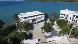 Un edificio moderno con techo plano, rodeado de vegetación y vistas despejadas al mar.