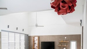 Amplia sala de estar con escalera de cristal, televisor de pantalla plana y un adorno rojo colgando del techo.
