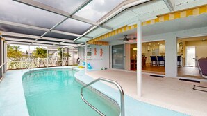 An indoor swimming pool with a glass ceiling, a children's play area, and a dining area visible through the glass doors.