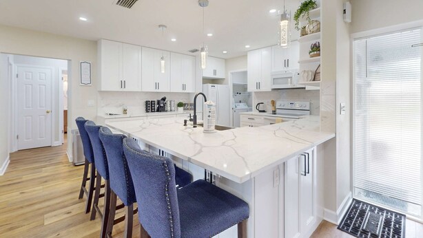 A modern kitchen with white cabinets, a marble island, and blue bar stools.