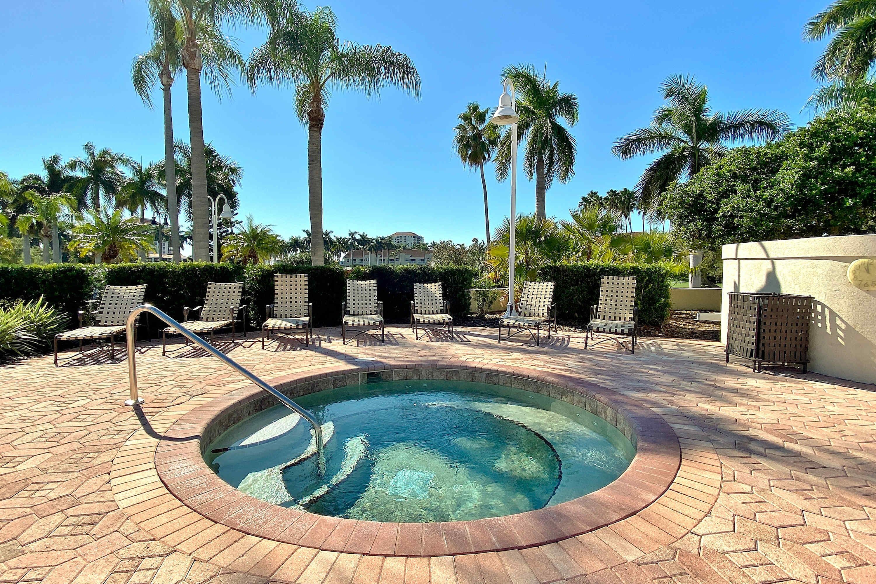 Un área de piscina con una piscina circular, sillas de descanso y palmeras.