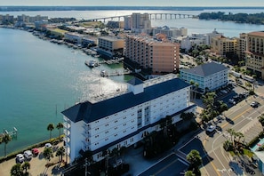 Un hotel costero de varios pisos, un puerto deportivo con barcos y un puente al fondo.
