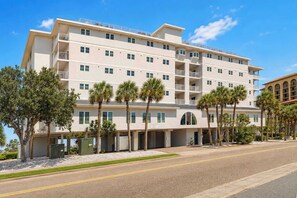 A multi-story hotel with a flat facade, balconies, and a parking area with palm trees.