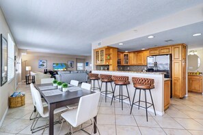 A modern kitchen with wooden cabinets, a stainless steel refrigerator, and a bar area with stools.