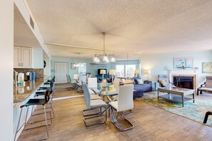 A spacious living room with a large dining table, comfortable seating, a fireplace, and a kitchen area with modern appliances. - Seashore getaway with partial Gulf view and beachfront heated pool and spa (Indian Shores)