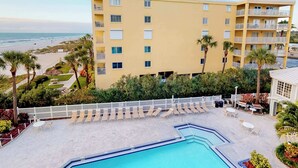 A hotel with a pool, lounge chairs, and a view of the beach.
