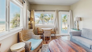A room with wicker furniture, a round table, and a sofa. There are large windows with curtains, a view of palm trees, and a beach. - Gulf front condo top floor beach access full kitchen and central AC (Indian Shores)