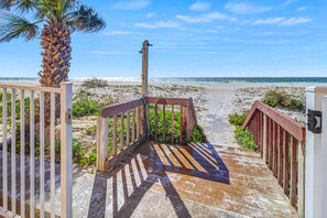 Un escalier en bois menant à une plage, avec un palmier et un ciel dégagé.