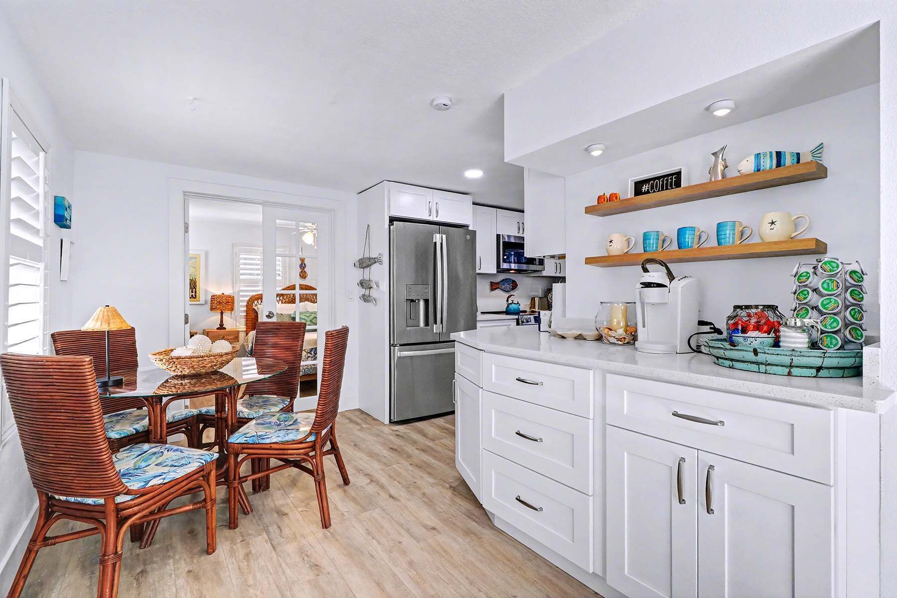 Una cocina moderna con armarios blancos, un refrigerador de acero inoxidable y una estación para café.