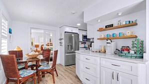 Una cocina moderna con armarios blancos, un refrigerador de acero inoxidable y una estación para café.