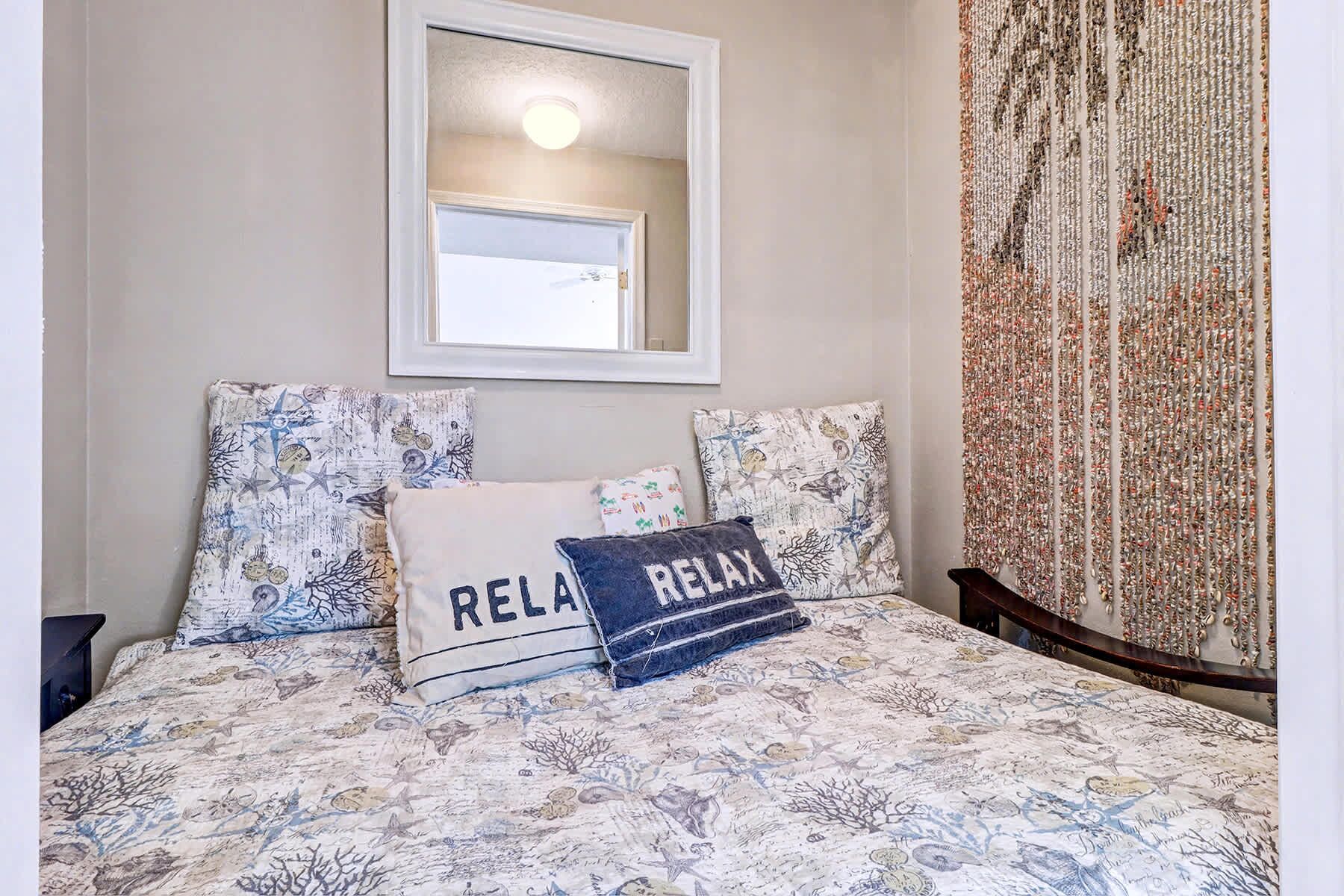 Un dormitorio con una cama, dos almohadas, una mesita de noche, un espejo y una cortina.