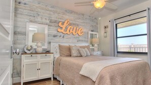Una camera da letto con un letto, un comodino, una cassettiera, una parete con la scritta 'Love', una finestra e una ventola a soffitto.