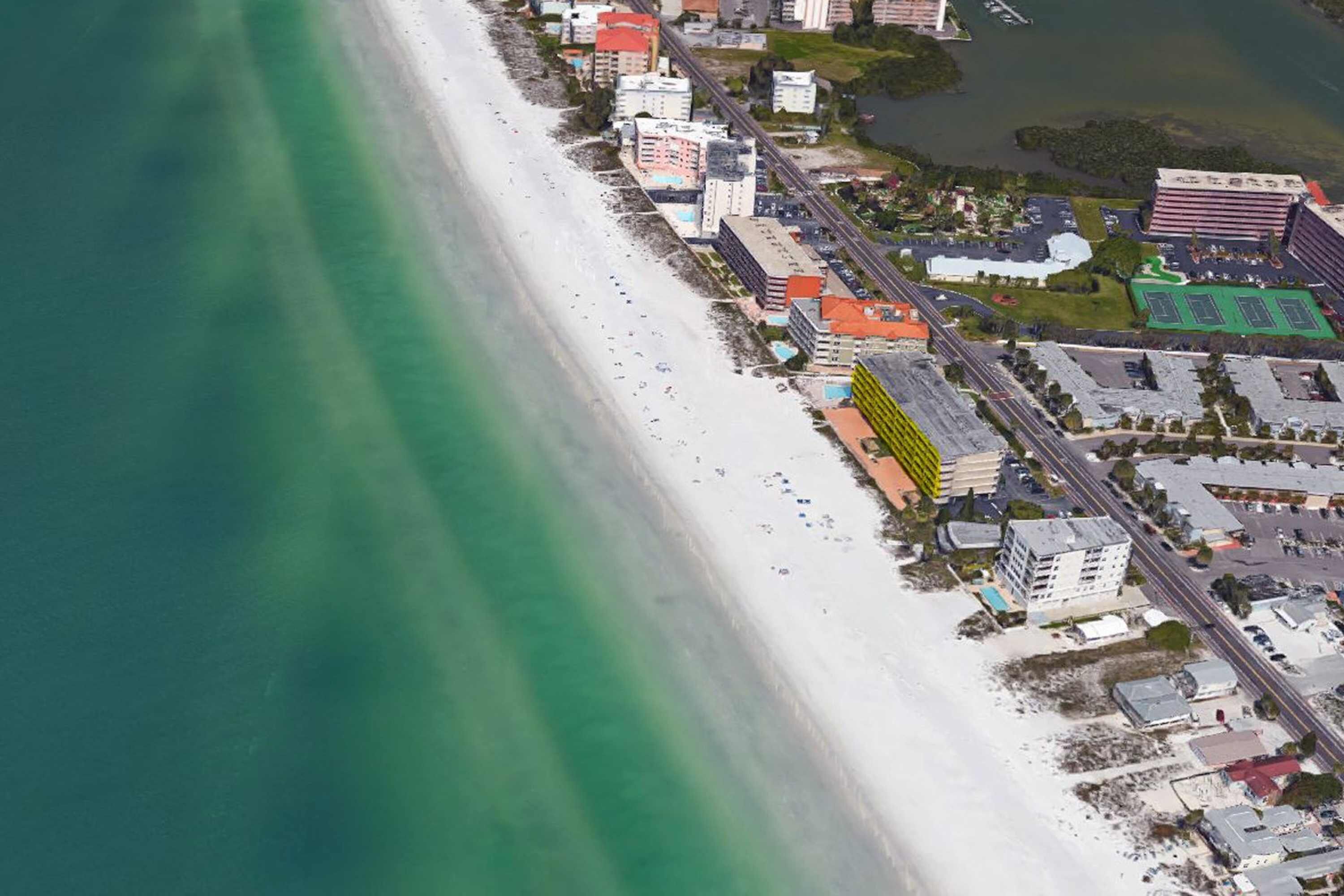 An aerial view of a coastal area with a beach, buildings, and a road.