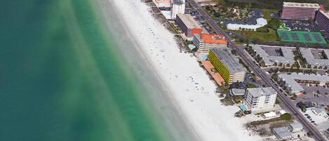 An aerial view of a coastal area with a beach, buildings, and a road.