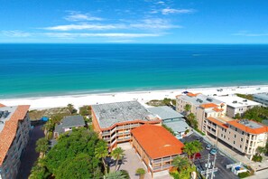 A beachfront hotel with multiple buildings, a parking area, and a view of the ocean.