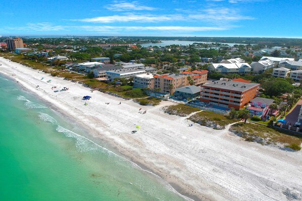An aerial view of a coastal area with a beach, buildings, and a distant body of water.