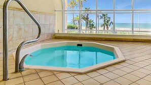 Une piscine avec un escalier en métal, une vue sur la plage à travers de grandes fenêtres et un revêtement de sol carrelé.