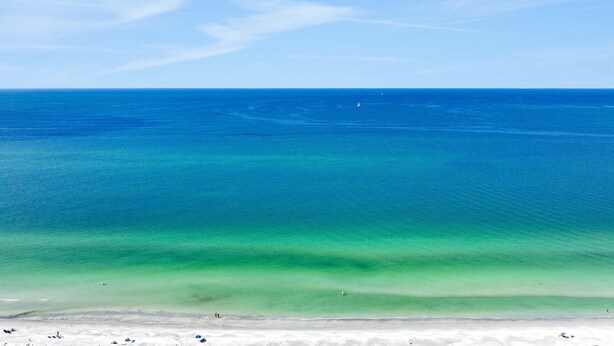 Une plage à l’eau turquoise et limpide, bordée d’un rivage sablonneux.